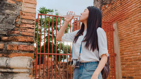 Young Asian backpacker woman blogger tourist with camera feel tired stand in front of pagoda take a rest and drink water in plastic bottle at old town , Lifestyle tourist travel holiday concept.の写真素材