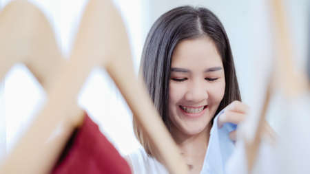 Beautiful attractive young Asian woman choosing her fashion outfit clothes in closet at home or store. Girl think what to wear sweater. Home wardrobe or clothing shop changing room.の写真素材