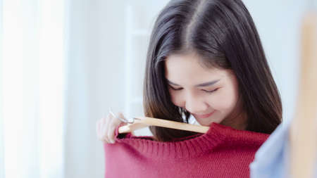 Beautiful attractive young Asian woman choosing her fashion outfit clothes in closet at home or store. Girl think what to wear sweater. Home wardrobe or clothing shop changing room.の写真素材