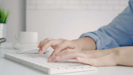 Beautiful young smiling Asian woman working on laptop while at home in office work space. Businesswoman working from home via portable computer writing on keyboard. Enjoying time at home.の写真素材