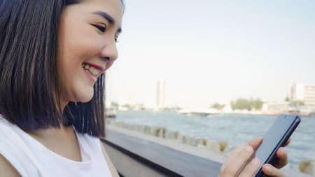 Tourist Asian women using mobile phone at outdoor cafe. Young Japanese Asia Girl using smartphone checking social media and texting with friends in social network enjoying the journey holiday travel.の写真素材