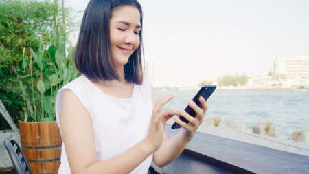 Tourist Asian women using mobile phone at outdoor cafe. Young Japanese Asia Girl using smartphone checking social media and texting with friends in social network enjoying the journey holiday travel.の写真素材