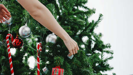 Asian female decorated with ornament on Christmas tree at Christmas and New Year festival at home. Xmas celebration event preparation or winter holidays festival indoor party concept. Close up shot.の写真素材