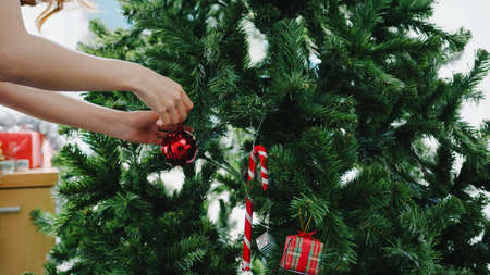 Asian female decorated with ornament on Christmas tree at Christmas and New Year festival at home. Xmas celebration event preparation or winter holidays festival indoor party concept. Close up shot.の写真素材