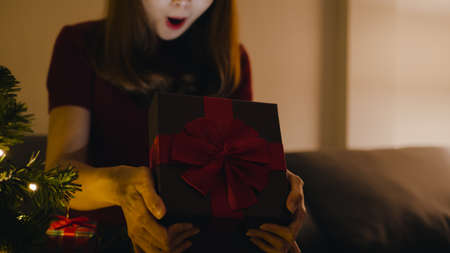 Young Asia female having fun opening X'Mas present box near Christmas tree decorated with ornaments in living room at home. Merry Christmas night and Happy New Year holiday festival.の写真素材
