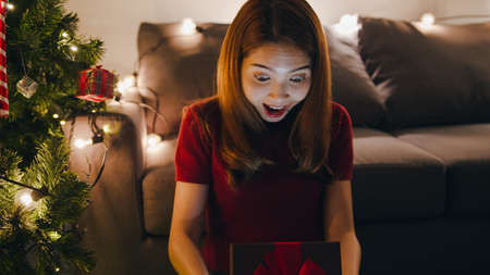 Young Asia female having fun opening X'Mas present box near Christmas tree decorated with ornaments in living room at home. Merry Christmas night and Happy New Year holiday festival.の写真素材