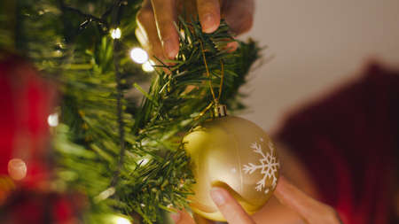 Asian female decorated with ornament on Christmas tree at Christmas night and New Year festival at home. Xmas celebration event preparation or winter holidays festival indoor party. Close up shot.の写真素材