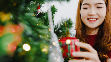 Asian female decorated with ornament on Christmas tree at Christmas and New Year festival in living...
