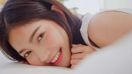 Asian woman smiling lying on bed in bedroom, Beautiful japanese female using relax time after wake up at home. Lifestyle women using relax time at home concept.の写真素材