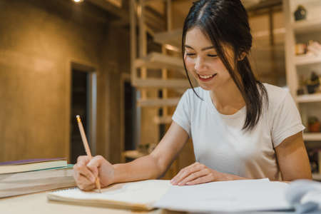 Asian student women reading books in library at university. Young undergraduate girl do homework, read textbook, study hard for knowledge on lecture desk at college campus overtime night.の写真素材