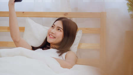 Young Asian teenager woman vlog at home, female using smartphone making vlog video to social media in bedroom. Lifestyle woman relax in morning at home concept.の写真素材