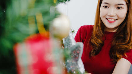 Asian female decorated with ornament on Christmas tree at Christmas and New Year festival in living room at home. Xmas celebration event preparation or winter holidays festival indoor party concept.の写真素材