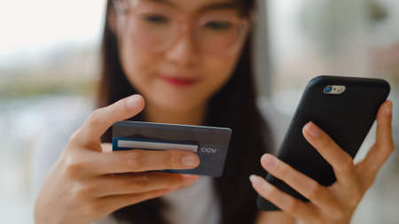 Freelance Asian women online shopping at coffee shop. Young Asia Girl using mobile phone, credit card buy and purchase e-commerce internet on table at outdoor cafe in the evening concept.の写真素材