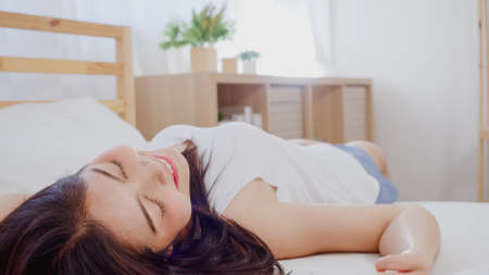 Beautiful attractive young Asian woman wake up, smiling and stretching her arms in her bed in bedroom. Young asia female use relax time at home. Lifestyle women relax at home concept.の写真素材