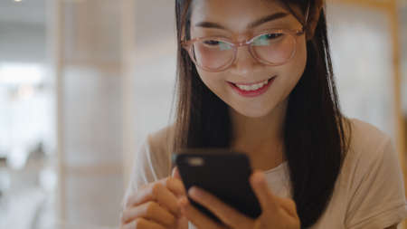 Freelance Asian women using mobile phone at office. Young Japanese Asia Girl using smartphone checking social media on the internet on the table at workplace concept.の写真素材