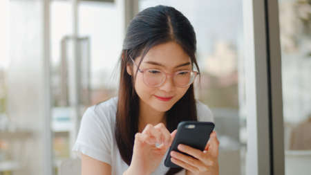 Freelance Asian women using mobile phone at a coffee shop. Young Asia Girl using smartphone checking social media internet on table at an outdoor cafe in the evening concept.の写真素材