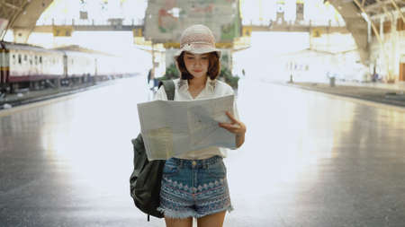Traveler backpacker Asian woman travel in Bangkok, Thailand. Happy young female direction and looking on location map at train station before travel.の写真素材