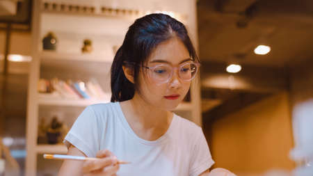 Asian student women reading books in library at university. Young undergraduate girl do homework, read textbook, study hard for knowledge on lecture desk at college campus overtime night.の写真素材