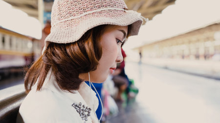 Happy teen Asian woman listening to the music with headphones and waiting in a train station summer. Travel Thailand concept.の写真素材
