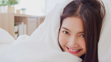 Asian woman smiling lying on bed in bedroom, Beautiful japanese female using relax time after wake up at home. Lifestyle women using relax time at home concept.の写真素材