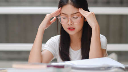 Asian student women read books in library at university. Young undergraduate girl stress tired have problem while study hard for knowledge on lecture desk at college campus concept.の写真素材