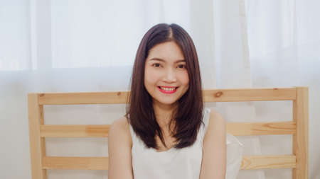 Teenager Asian woman feeling happy smiling and looking to camera while relax in bedroom at home. Lifestyle beautiful Asian young female using relax time at home concept.の写真素材