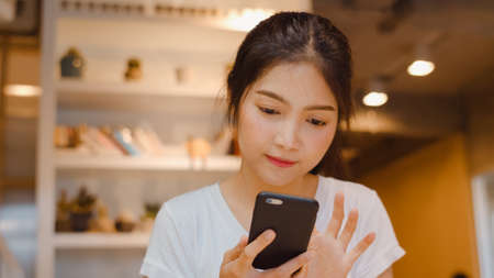 Freelance Asian women using mobile phone at office. Young Japanese Asia Girl using smartphone checking social media on the internet on the table at workplace concept.の写真素材