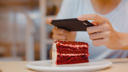 Blogger Asian friendly women influencer eat cake at night cafe. Beautiful young lady happy relax fun using technology mobile phone taking a photo of her food upload in social media at college campus.の写真素材