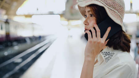 Traveler backpacker Asian woman travel in Bangkok, Thailand. Happy young female using smartphone for talking, reading and texting at train station.の写真素材