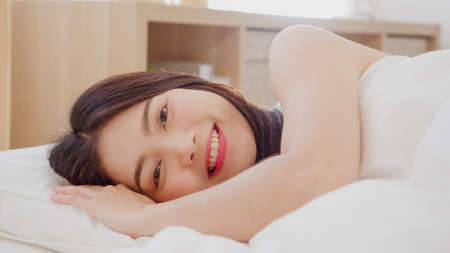 Asian woman smiling lying on bed in bedroom, Beautiful japanese female using relax time after wake up at home. Lifestyle women using relax time at home concept.の写真素材