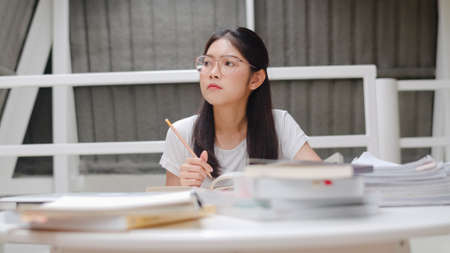 Asian student women reading books in library at university. Young undergraduate girl do homework, read textbook, study hard for knowledge and education on lecture desk at college campus.の写真素材