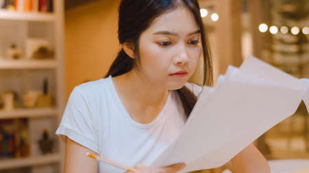 Asian student women reading books in library at university. Young undergraduate girl do homework, read textbook, study hard for knowledge on lecture desk at college campus overtime night.の写真素材