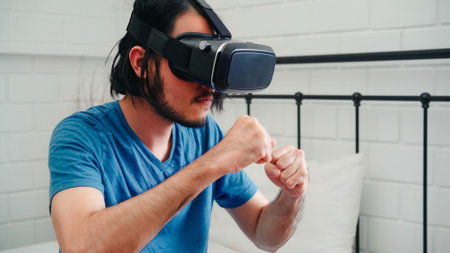 Young Asian man using glasses virtual reality simulator playing boxing game in bedroom, Japanese male feeling happy using relax time lying on bed at home. Teen play games relax at home concept.の写真素材