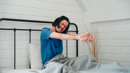Young Asian man wake up in the morning, male stretching after awake on bed in bedroom at home. Handsome men nap, sleepy relax in modern house concept.の写真素材