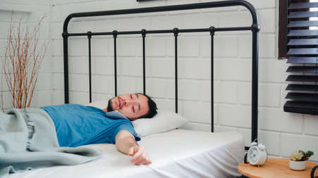 Young Asian man wake up in the morning, Asia male talking with friends on mobile phone after awake on bed in bedroom at home. Handsome men nap, sleepy relax in modern house concept.の写真素材