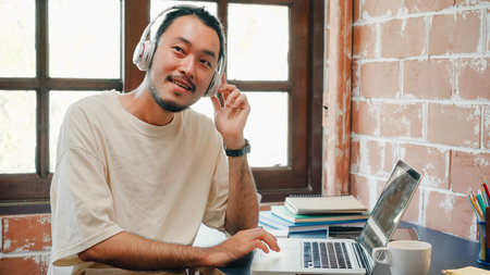 Freelance Asia guy headphones listening music and working on laptop in living room at house in the morning. Working from home, remotely work, social distancingの写真素材