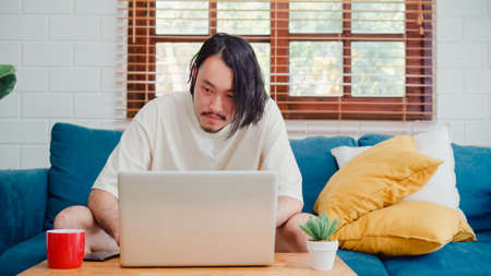 Freelance Asia guy working at his desk in office taking a call on his mobile phone while writing notes on a notepad. Working from home, remotely work, social distancing, quarantine for coronavirus.の写真素材