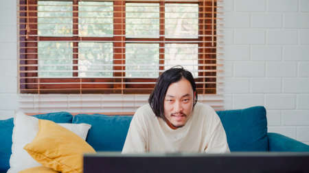 Freelance Asia guy working at his desk in office taking a call on his mobile phone while writing notes on a notepad. Working from home, remotely work, social distancing, quarantine for coronavirus.の写真素材
