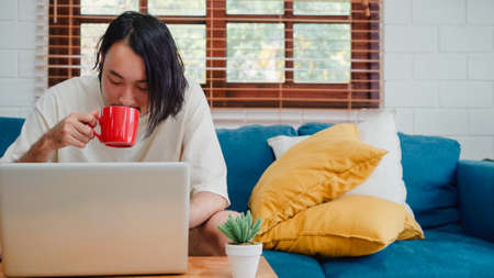 Freelance Asia guy working at his desk in office taking a call on his mobile phone while writing notes on a notepad.の写真素材