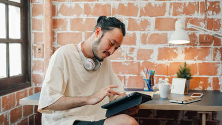 Freelance Asia guy working at his desk in office taking a call on his mobile phone while writing notes on a notepad.の写真素材