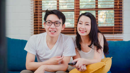 Asian couple watching television in living room at home, sweet couple enjoy love moment while lying on the sofa when relaxed at home. Lifestyle couple relax at home concept.の写真素材