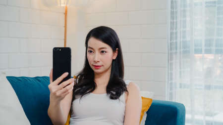 Asian influencer women using camera streaming and recording vlog video about the benefit of drinking milk and sandwiches for breakfast on sofa in living room at home for broadcast online.の写真素材