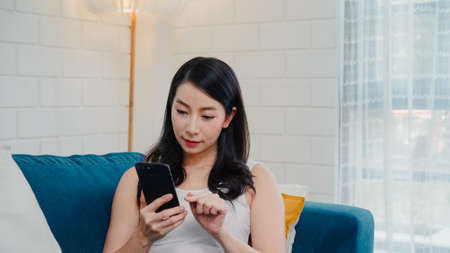 Asian influencer women using camera streaming and recording vlog video about the benefit of drinking milk and sandwiches for breakfast on sofa in living room at home for broadcast online.の写真素材