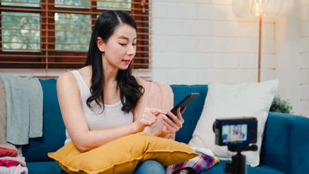 Asian influencer women using camera streaming and recording vlog video about the benefit of drinking milk and sandwiches for breakfast on sofa in living room at home for broadcast online.の写真素材