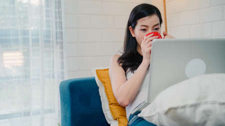 Asian influencer women using camera streaming and recording vlog video about the benefit of drinking milk and sandwiches for breakfast on sofa in living room at home for broadcast online.の写真素材