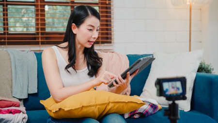 Asian influencer women using camera streaming and recording vlog video about the benefit of drinking milk and sandwiches for breakfast on sofa in living room at home for broadcast online.の写真素材