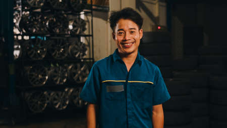 Professional car mechanic screwing details of car engine on lifted automobile at repair service station. Skillful Asian guy in uniform fixing car at mechanics garage at night.の写真素材