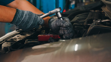 Professional car mechanic screwing details of car engine on lifted automobile at repair service...