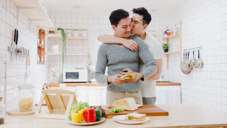 Young Asia gay couple propose at modern home, LGBTQ men happy smiling have romantic time while proposing and marriage surprise wear wedding ring in living room at house. Anniversary romantic concept.の写真素材
