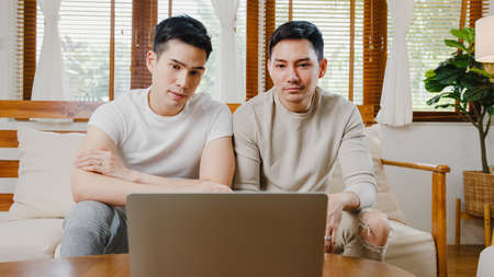 Young Asia gay couple propose at modern home, LGBTQ men happy smiling have romantic time while proposing and marriage surprise wear wedding ring in living room at house. Anniversary romantic concept.の写真素材